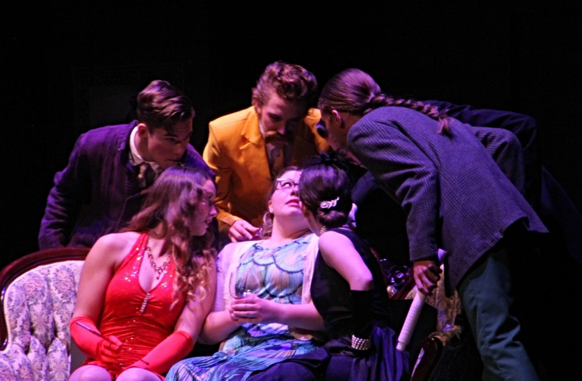 The cast leans in on Sophia Shinka (Mrs. Peacock) in accusation. 