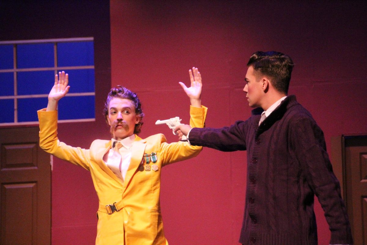 Sam Hannig (Colonel Mustard) throws up his hands while being held at gunpoint by Zack Binkley (Professor Plum). 