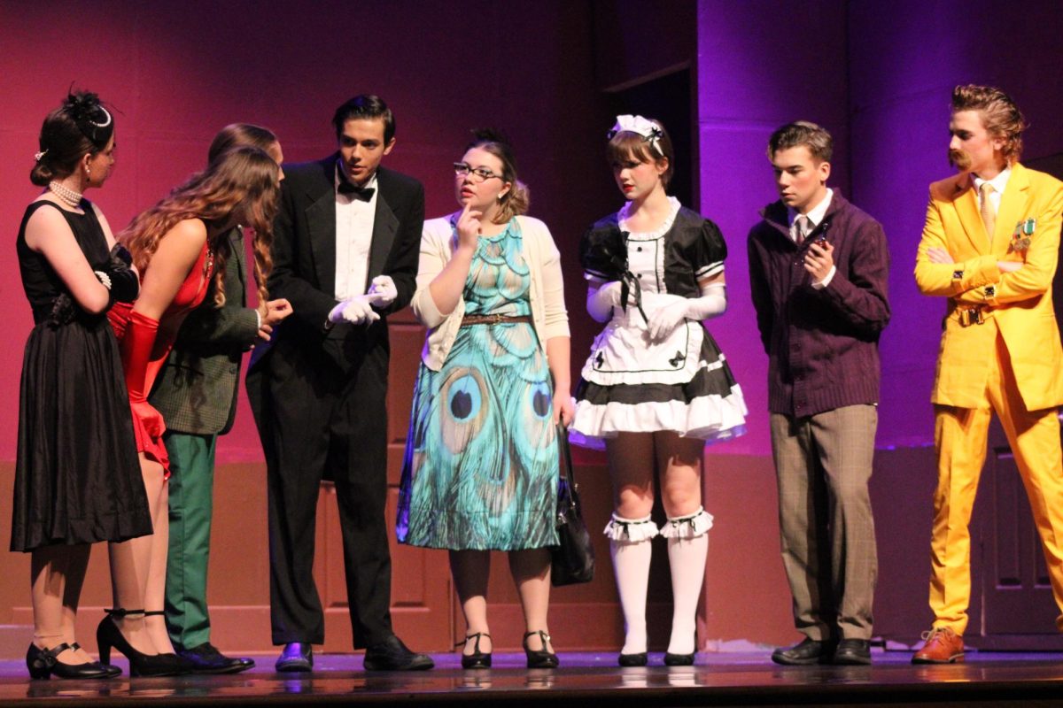 Senior Lani Casto (Mrs. White), senior Jordyn York (Miss Scarlet), junior Max Holtsberry (Mr. Green), junior Owen Costa (Wadsworth), senior Sophia Shinka (Mrs. Peacock), junior Eon Walters (Yvette), senior Zach Binkley (Professor Plum) and junior Sam Hannig (Colonel Mustard) gather around to formulate a hypothesis about who the murderer is. 