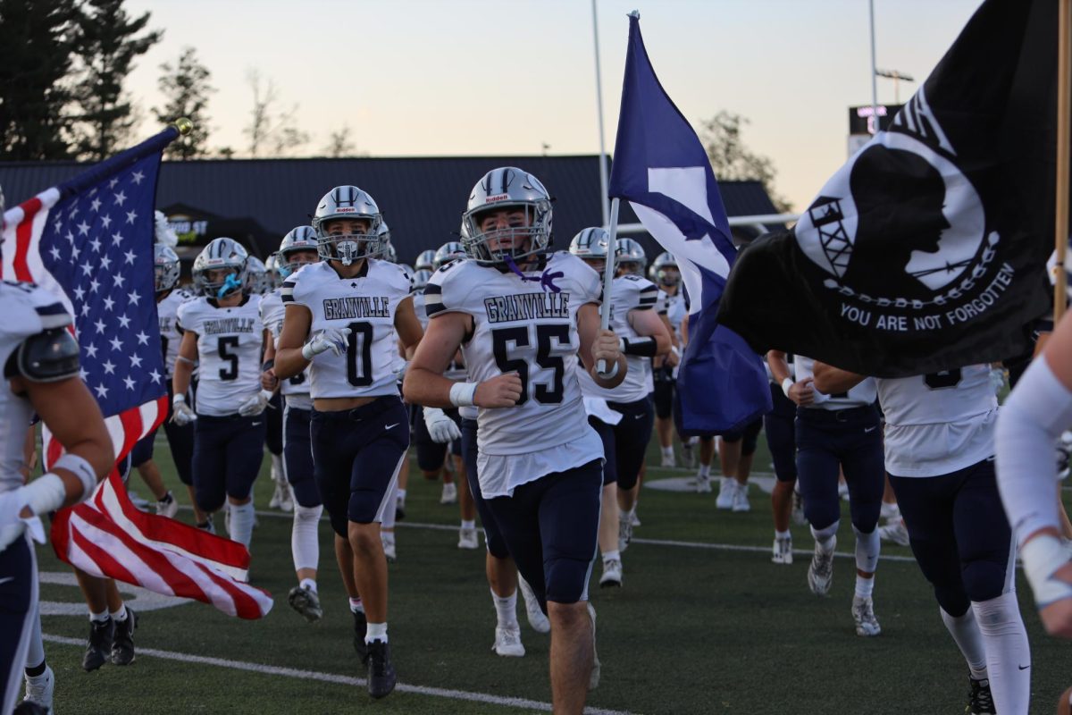 Rory McShane (12) runs out carrying the Aces flag on Watkins Memorial turf to defend Granville. 