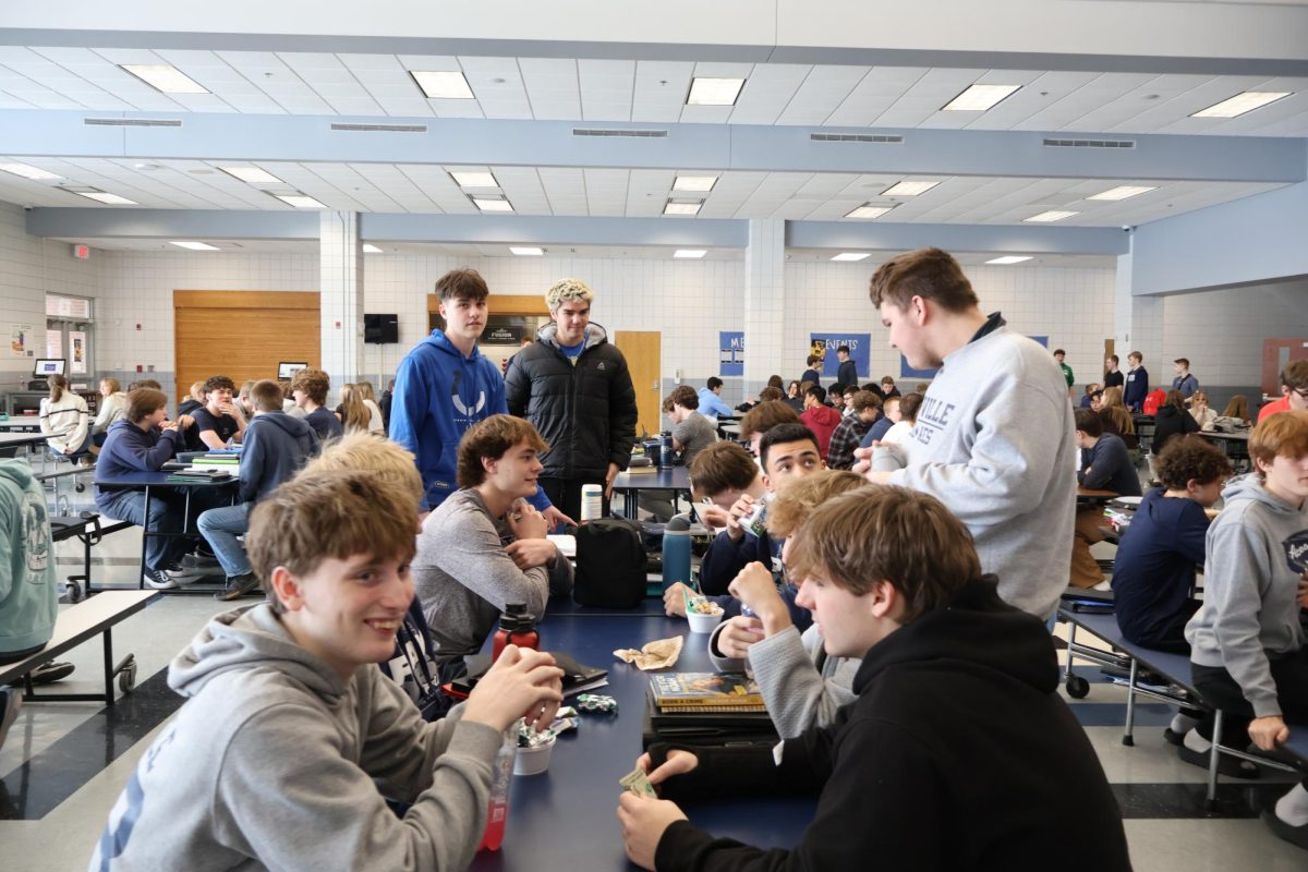 Sophomore boys sixth period lunch table laughs together while they eat without any devices. 