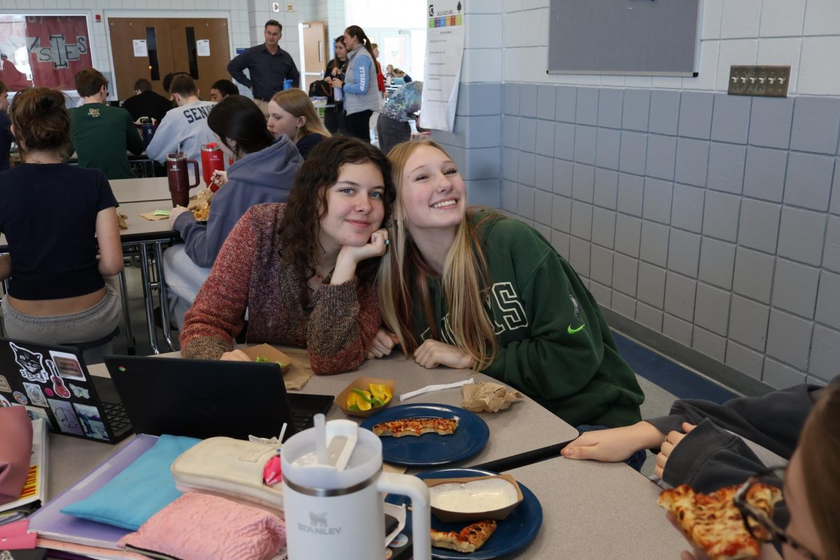 Sophomores Gigi Stone and Elvi Kelly pose happily for a photo and continue to work on a project while at lunch. 