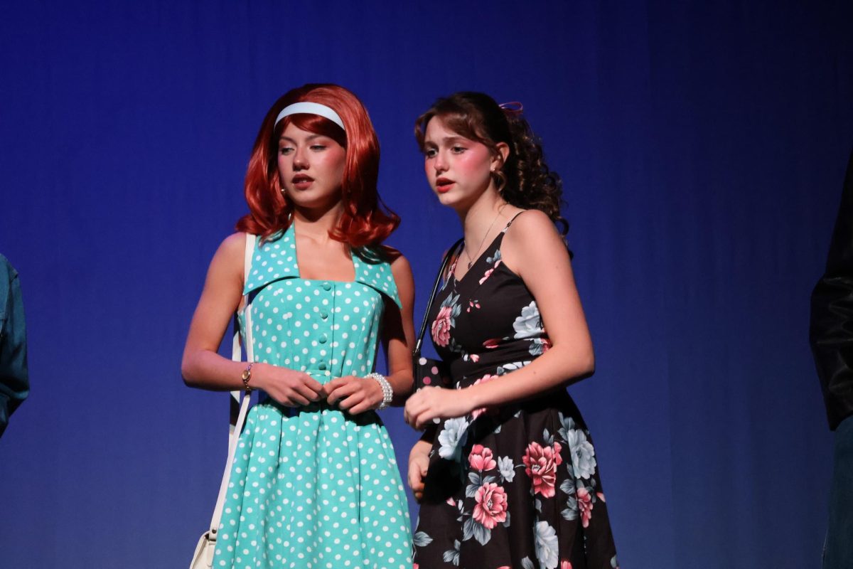 Cherry (Clara Dandurand) and Marsha (Ava Whitmyer) discuss with each other about how they feel about talking with the greasers.