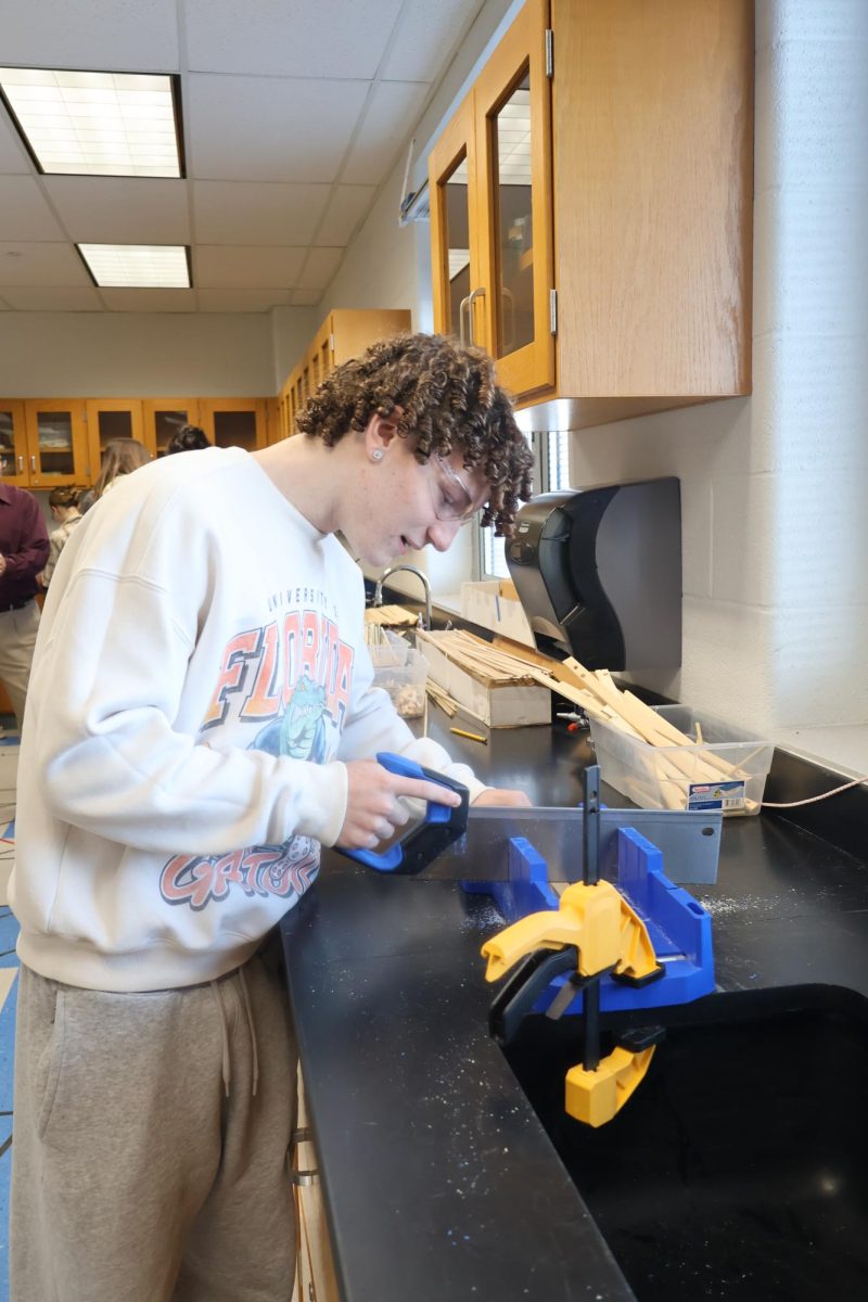 Sophomore Trey Curry uses a saw cutting wood to start the base for his car. Trey and his partner Jackson Hicks had an idea outside of the box that ended up succeding. 