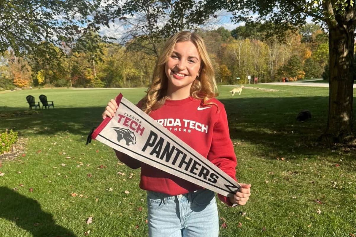 Grace Largent smiles in a Florida Tech sweatshirt, holding a Florida Tech pennant flag to showcase her swimming commitment. Photo courtesy of Grace Largent.  